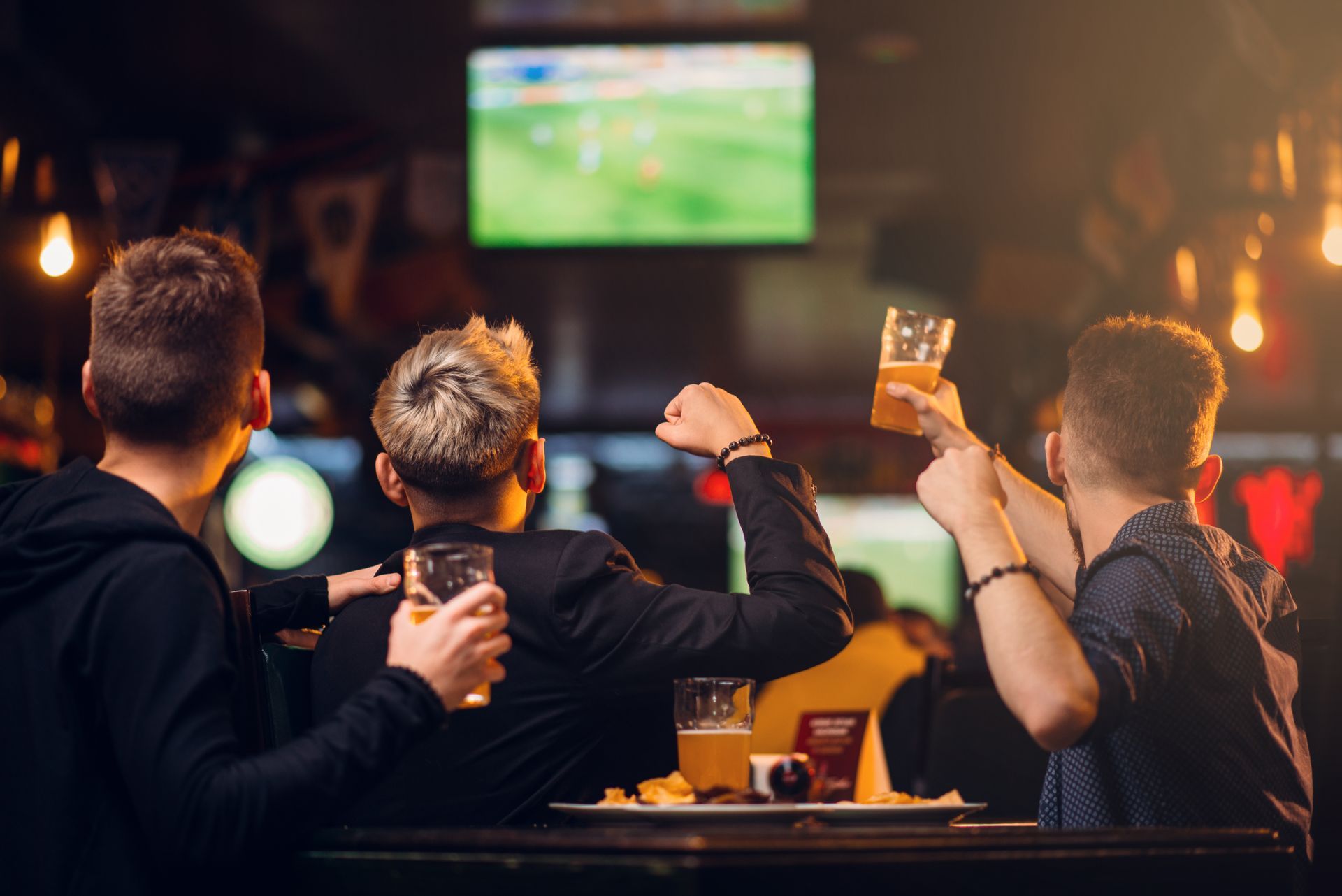 People cheering and raising drinks in a dim bar while watching a sports game on TV