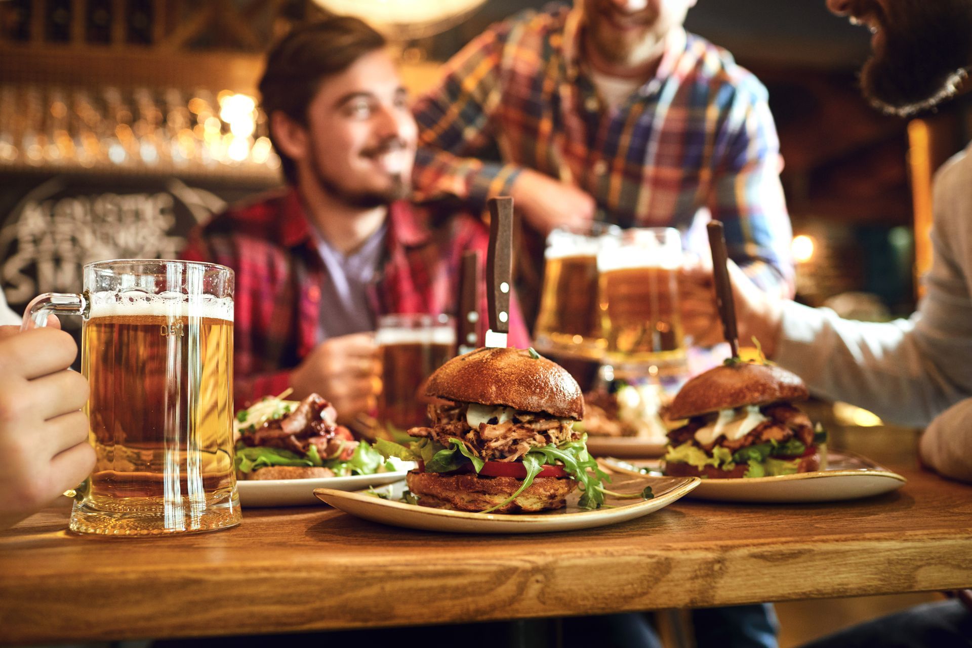 Friends at a pub, eating burgers, drinking beer. Wooden table, happy expressions, dim lighting.