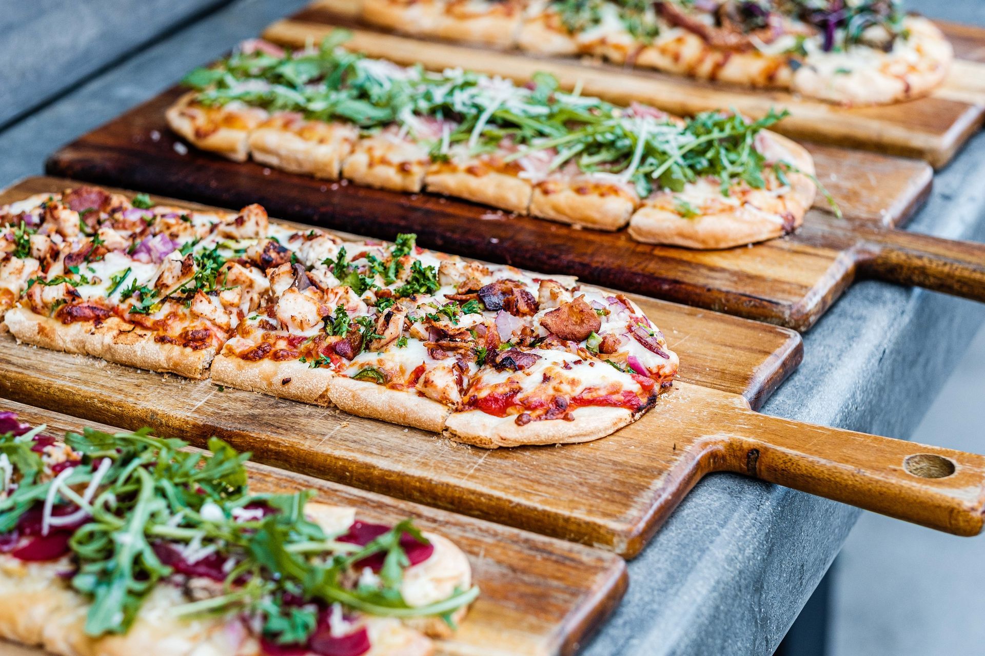 Flatbread pizzas on wooden serving boards, assorted toppings, outdoor setting.