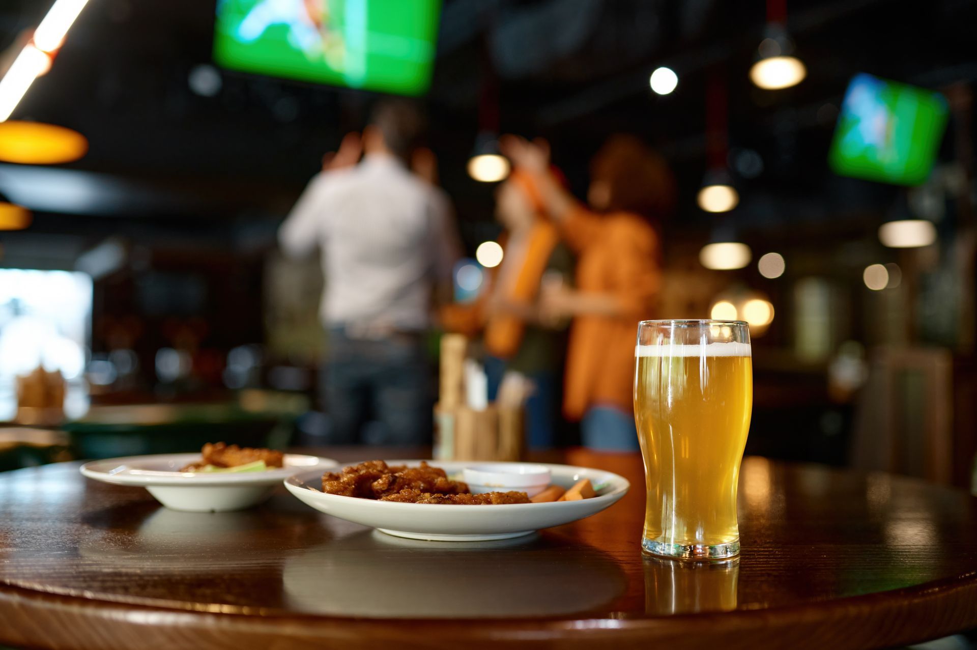 Beer and snacks on a table in a bar; people cheering in the background.