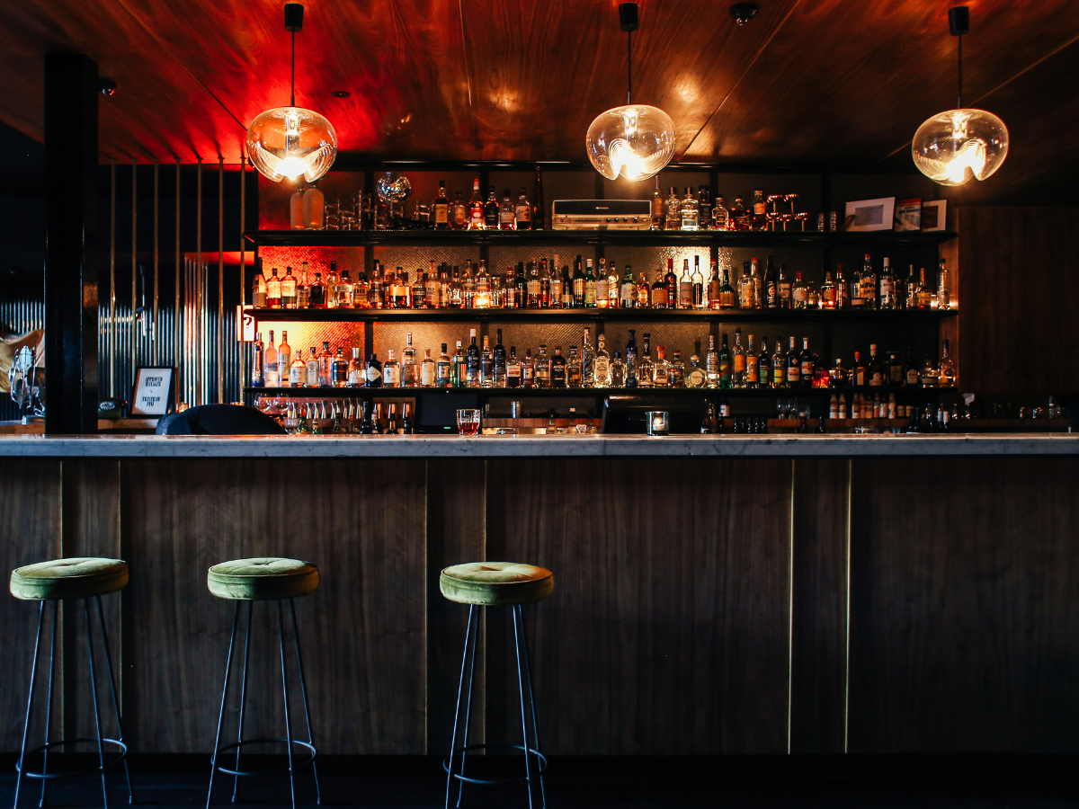 A bar with stools and shelves full of liquor