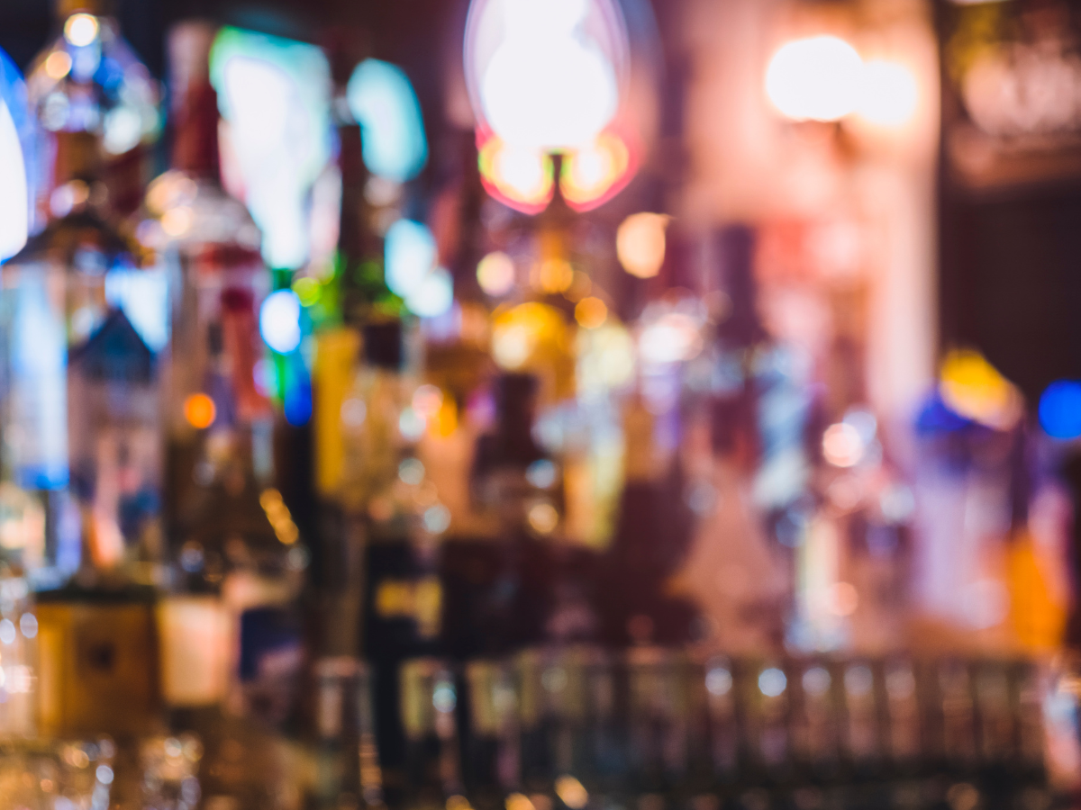A blurred photo o glasses lined p infront of a bar
