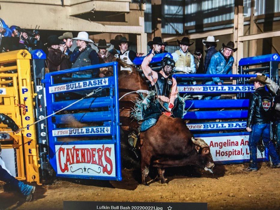 Bull rider on a bucking bull at an arena. Cavender's and Angelina Arts Hospital logos visible. Blue and yellow barriers.