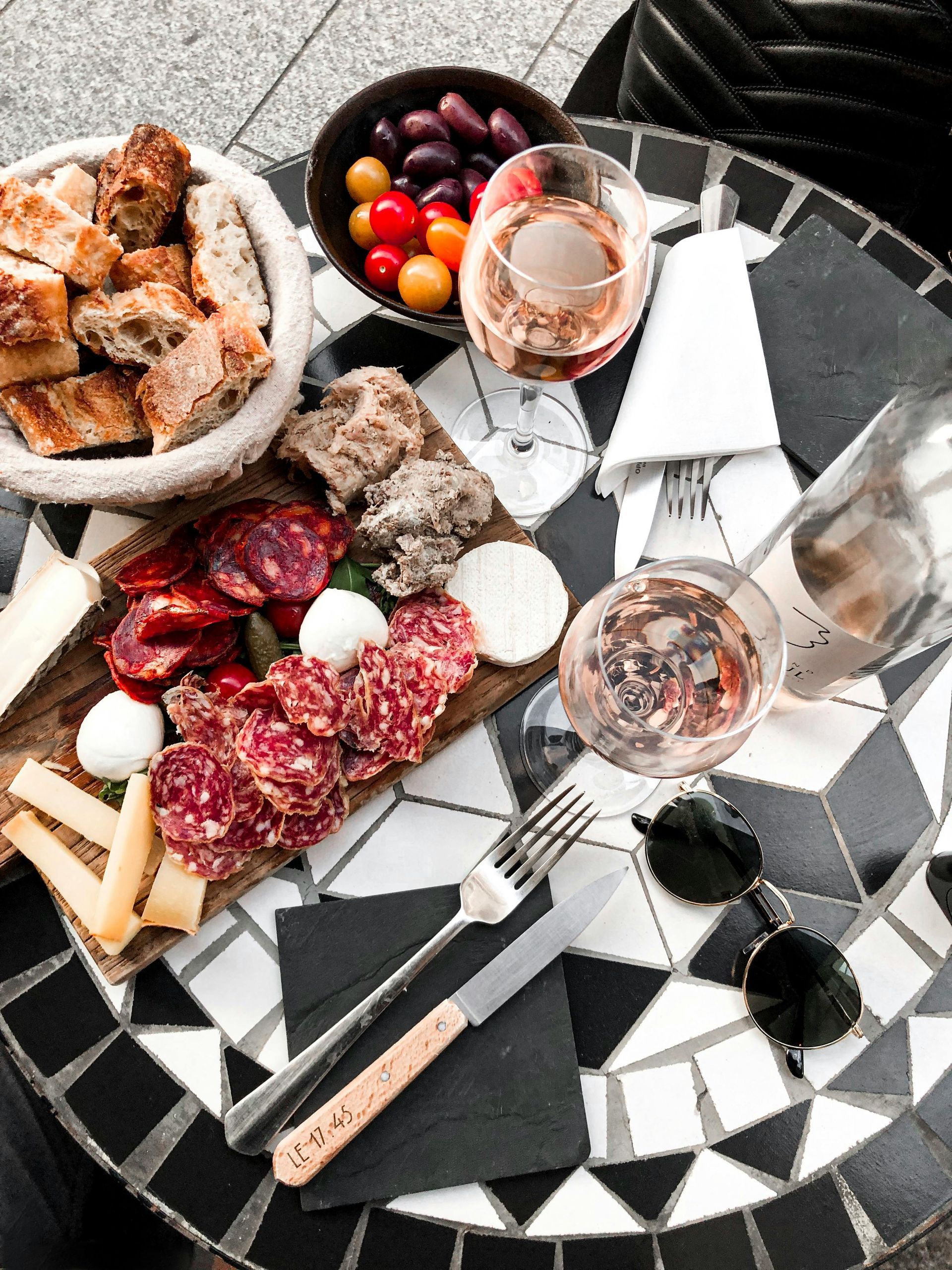 Charcuterie board with salami, cheese, olives, and wine on a mosaic table.