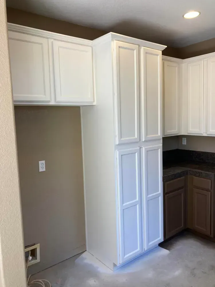 White kitchen cabinets against a tan wall, with a laundry hookup and brown and white countertops.