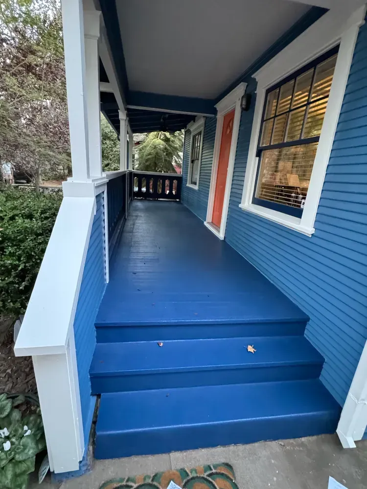 Blue painted porch with steps, white trim, and an orange door.