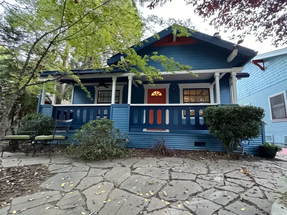 Blue Craftsman-style house with red door, porch, and stone walkway. Trees surround the house.