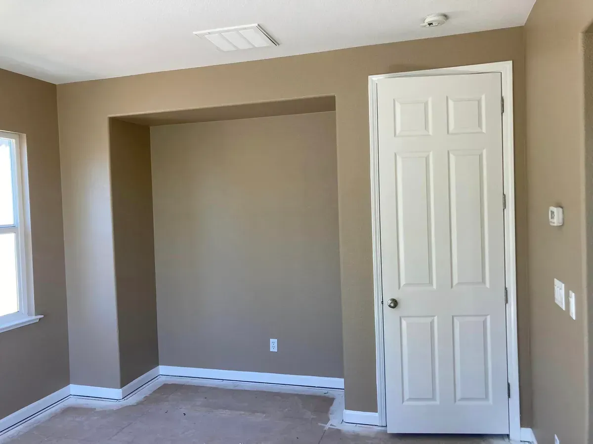 Empty bedroom with a recessed wall, white door, and beige walls.
