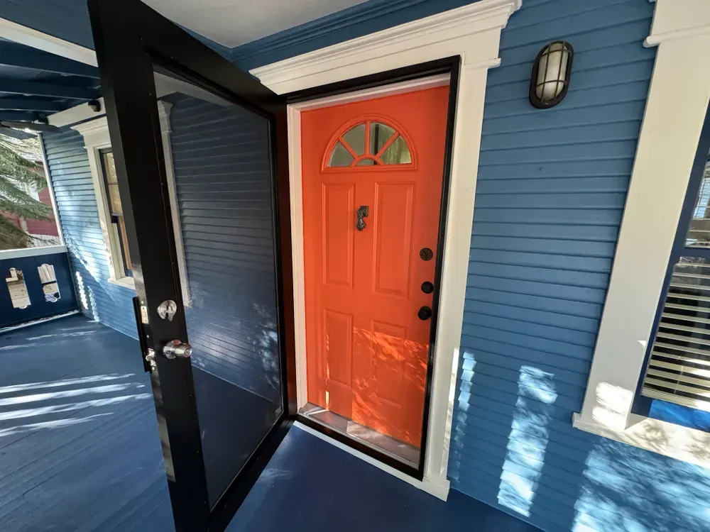Bright orange front door with black screen door on blue house porch.
