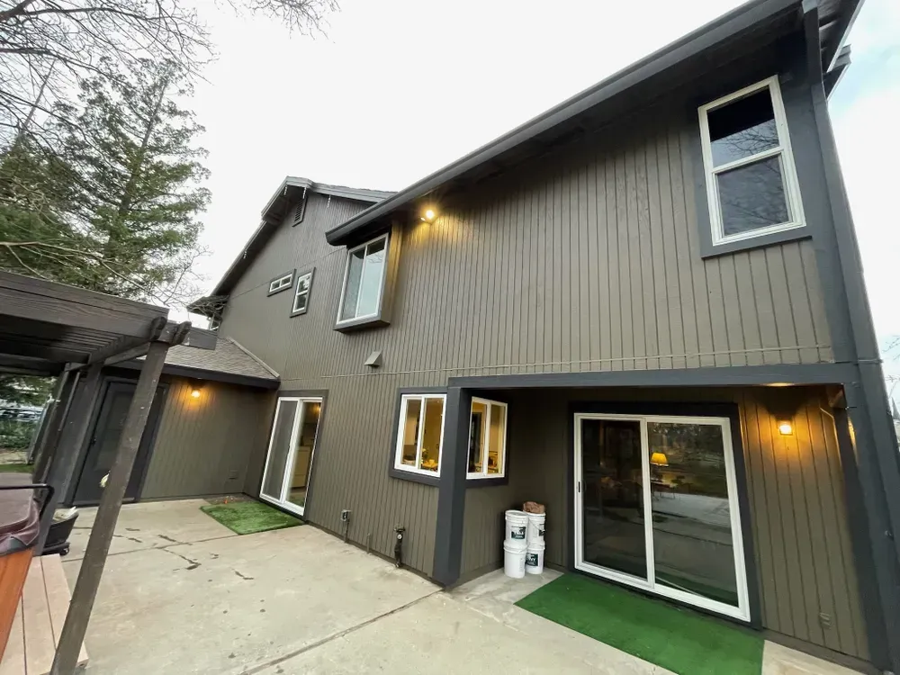Exterior of a two-story house with brown siding and white-framed windows. Patio in front.