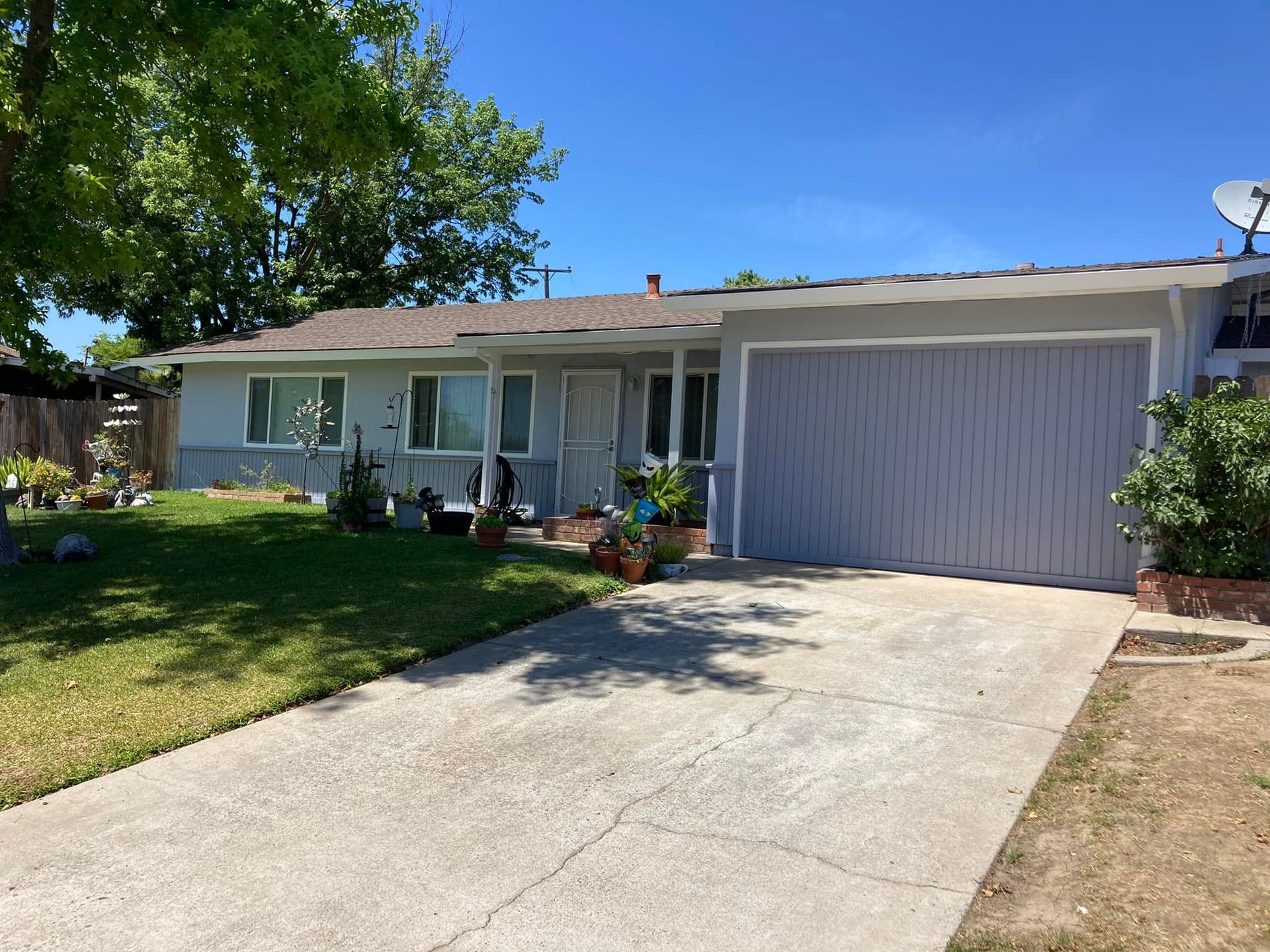 Gray ranch-style house with a light blue garage door, on a sunny day. Green lawn and driveway in front.