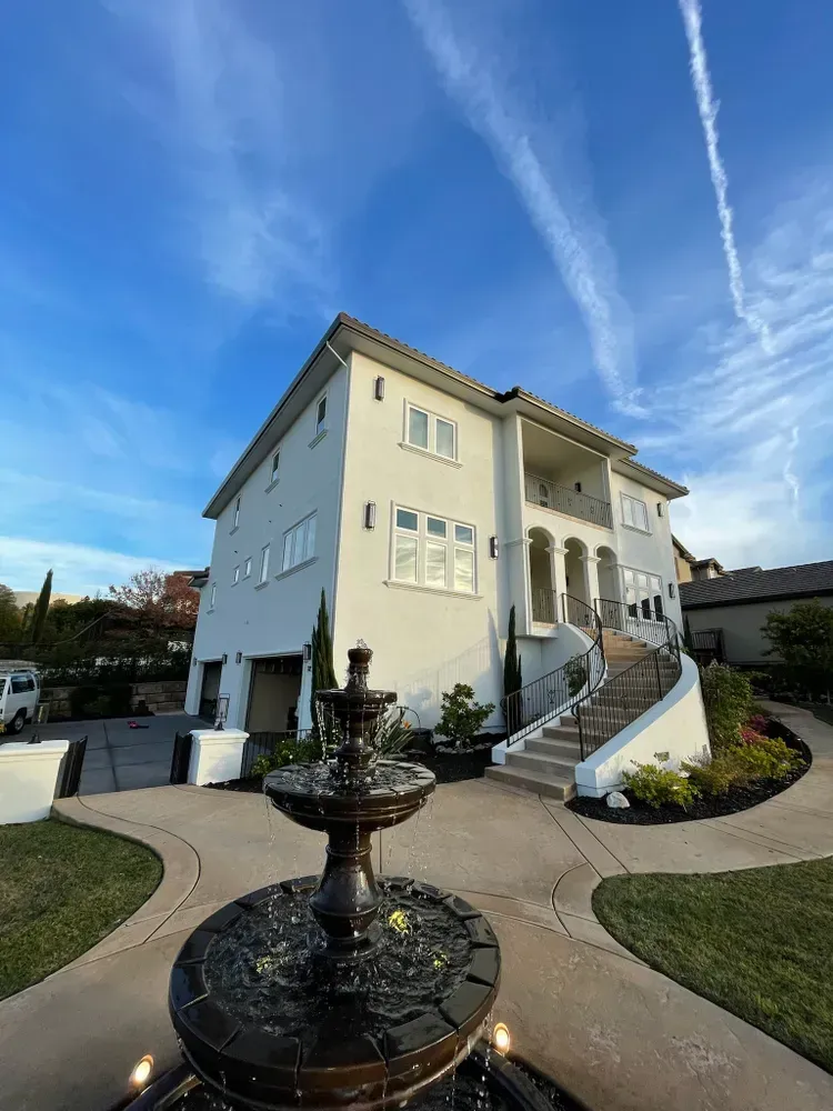 Three-story white house with fountain in front on a sunny day with blue sky and contrails.