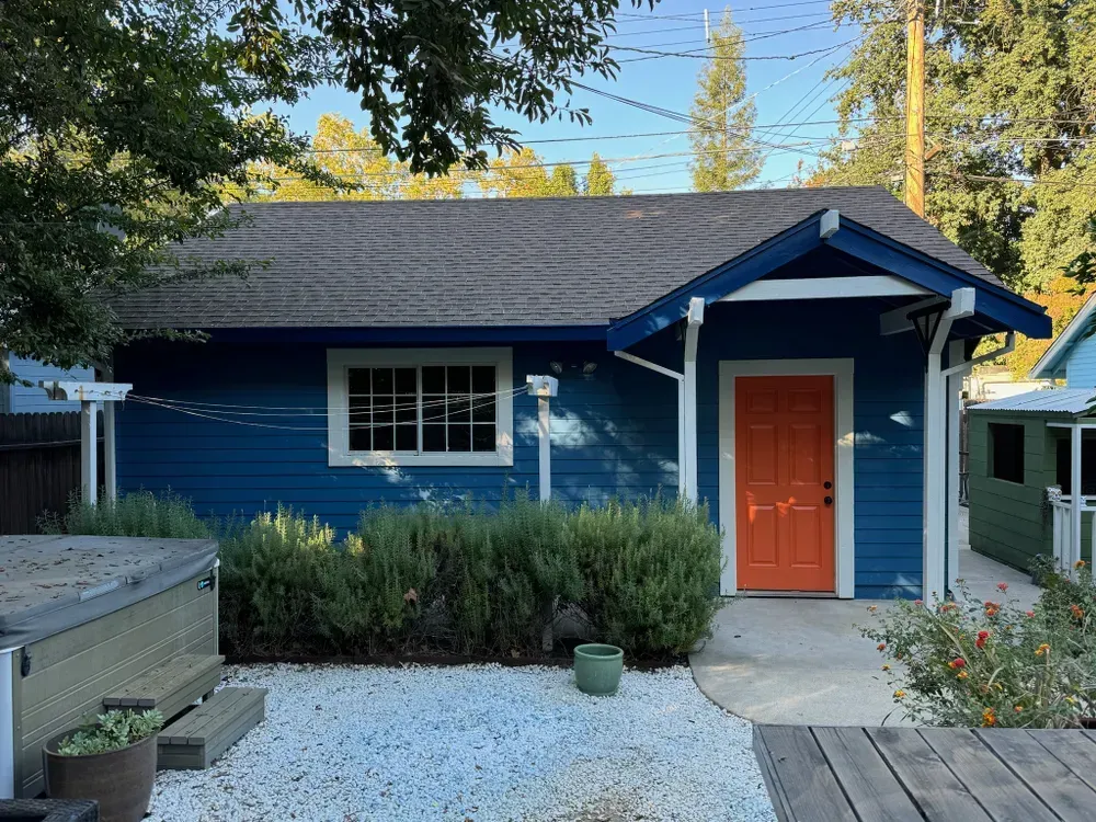 Blue cottage with an orange door, white trim, and a rock yard.
