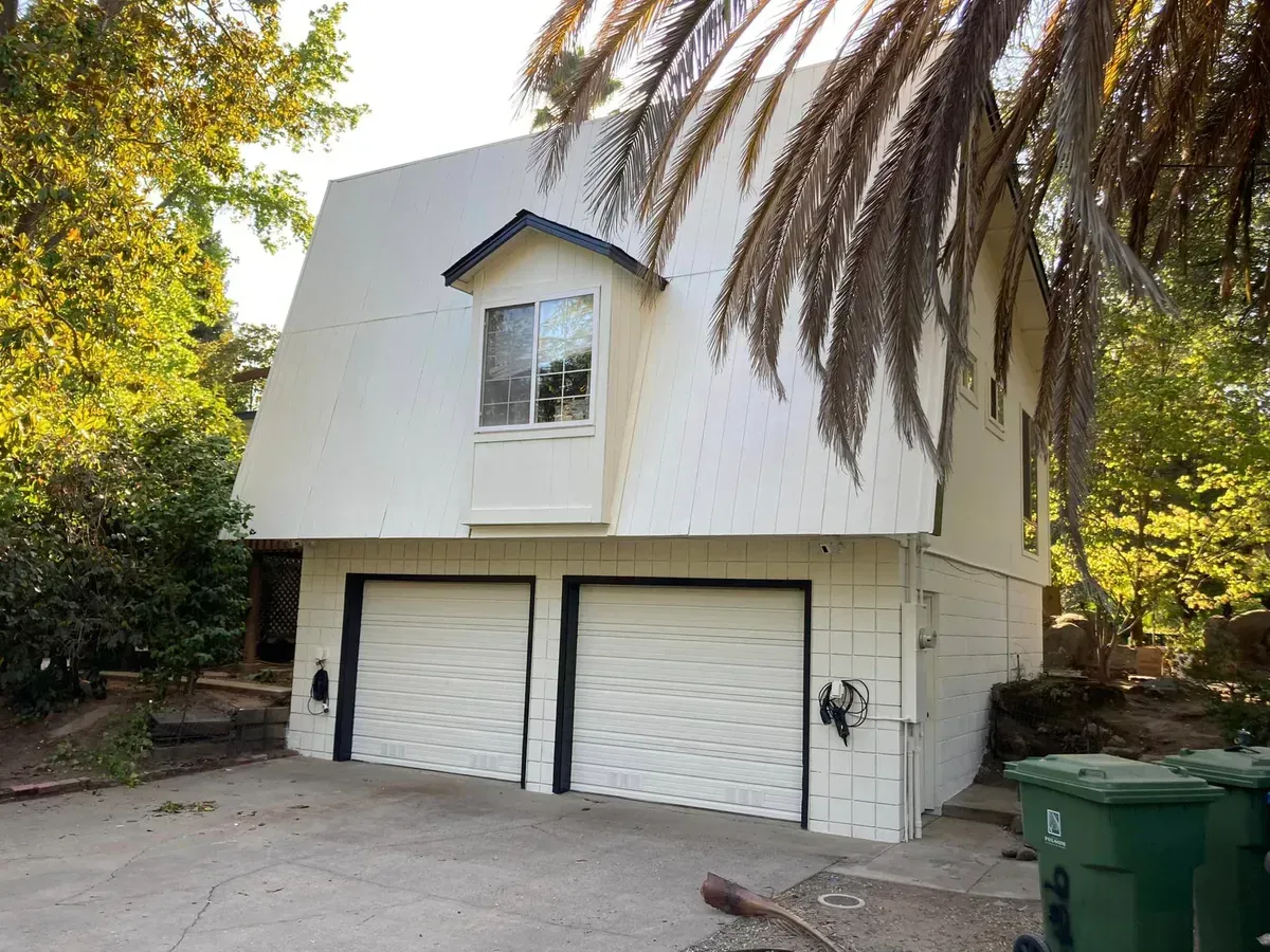Two-story white building with garage doors, small window, and trees.