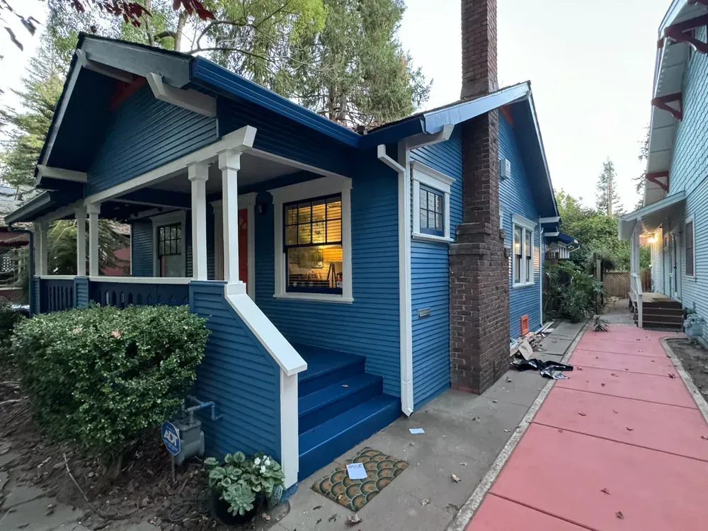Blue house with white trim and front porch. Brick chimney, steps, and red sidewalk.