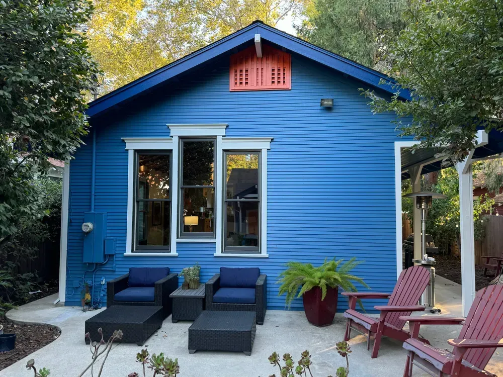 Blue house with outdoor seating; red chairs, dark blue cushions, and green plants on a patio.