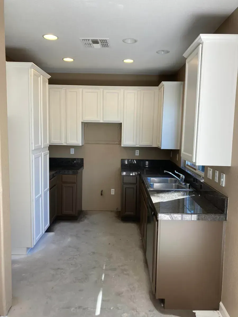 A kitchen with white upper cabinets, brown lower cabinets, and dark countertops under construction.