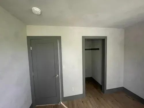 Bedroom interior with gray trim, door, and closet, gray walls, wood floor, and smoke detector.