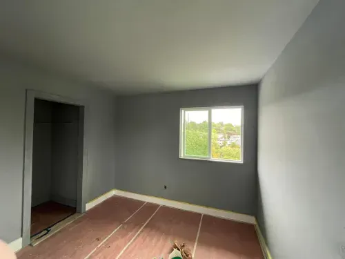 Empty bedroom with gray walls, a window, and unfinished wood flooring.