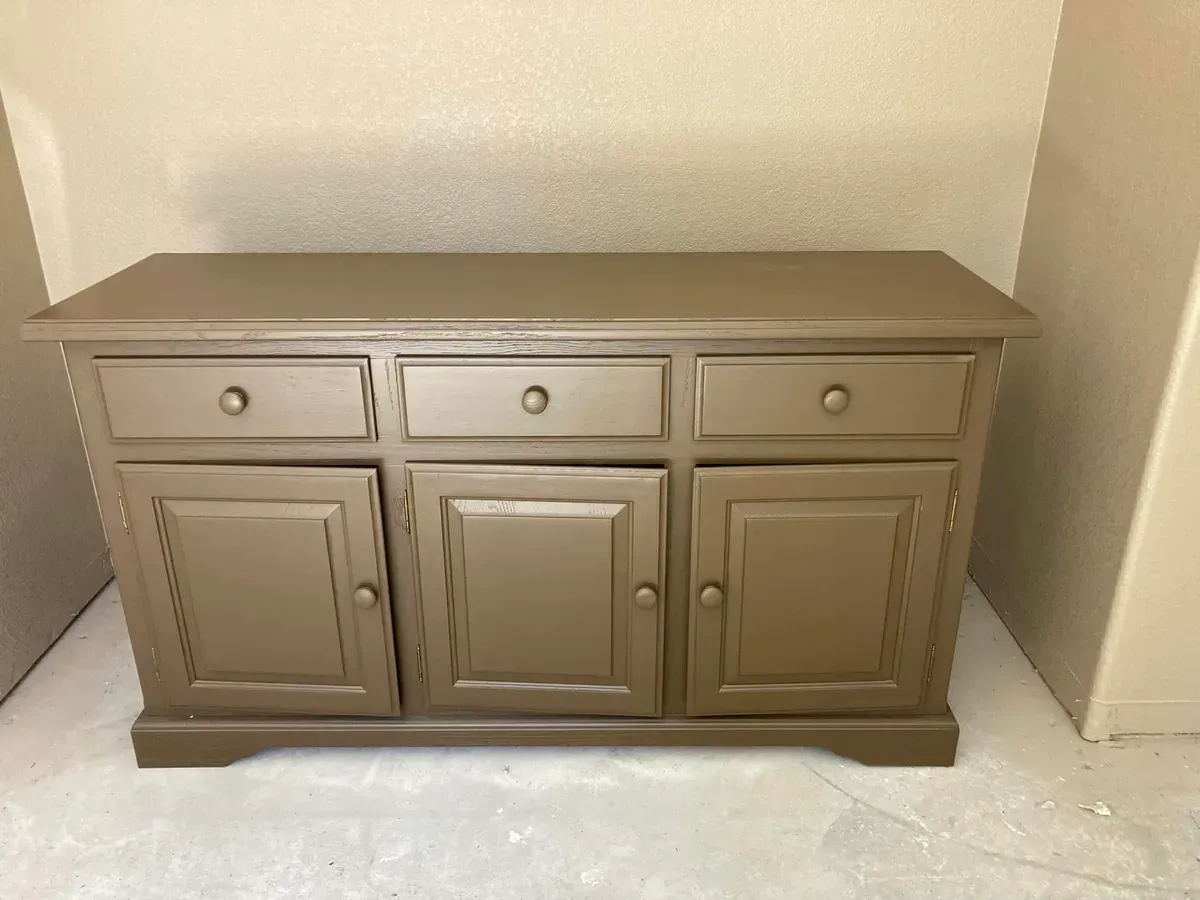 Brown painted buffet with drawers and cabinet doors against a beige wall.