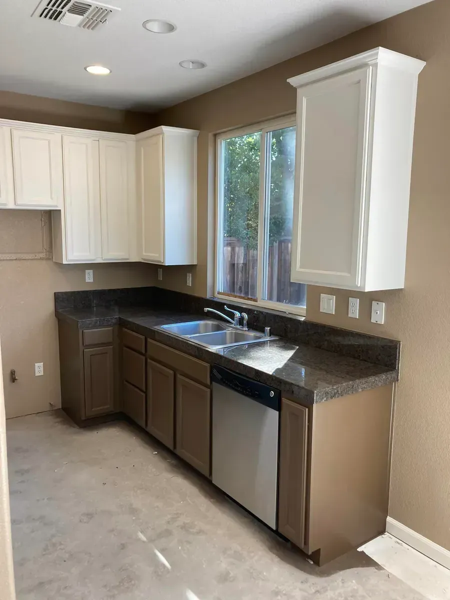 Kitchen with white upper cabinets, brown lower cabinets, granite countertops, and a stainless steel dishwasher.