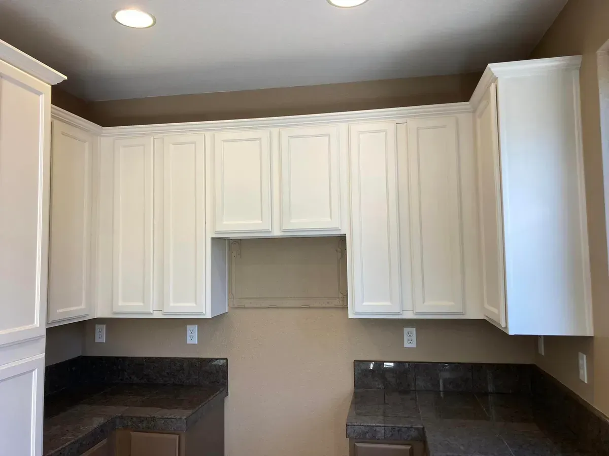 Cream-colored kitchen cabinets with dark countertops against a beige wall; two recessed lights overhead.