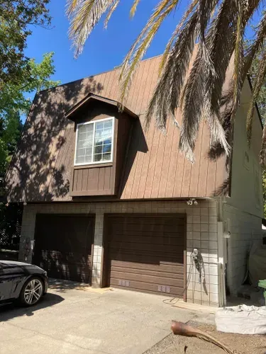 Two-story house with brown garage doors, dormer window, and palm trees.