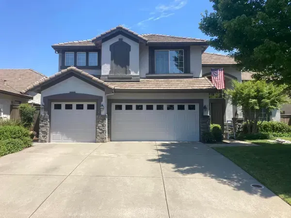 Two-story house with garage, stone accents, concrete driveway, and an American flag hanging.