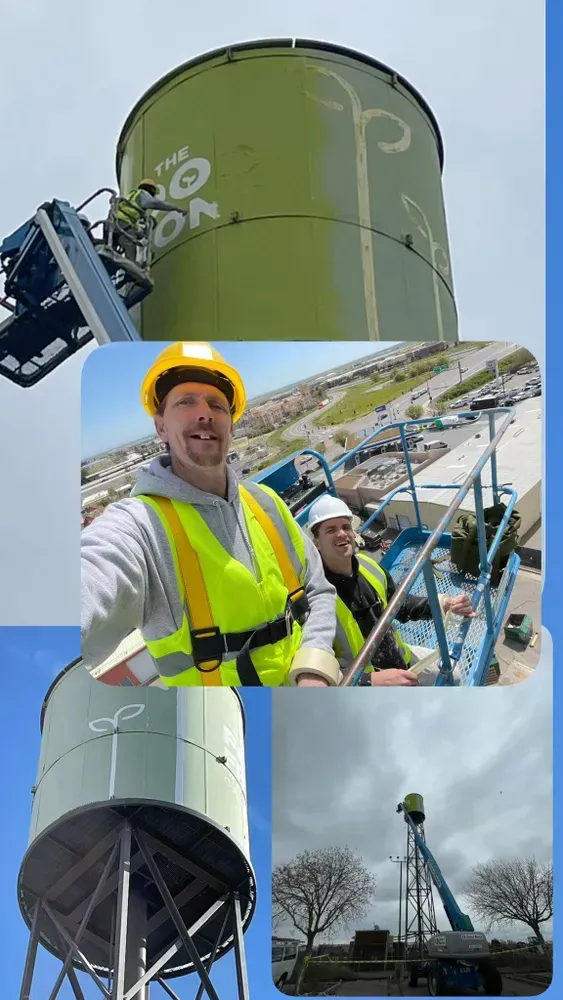 Workers painting a tall, green water tower. One worker takes a selfie. Clear blue sky.