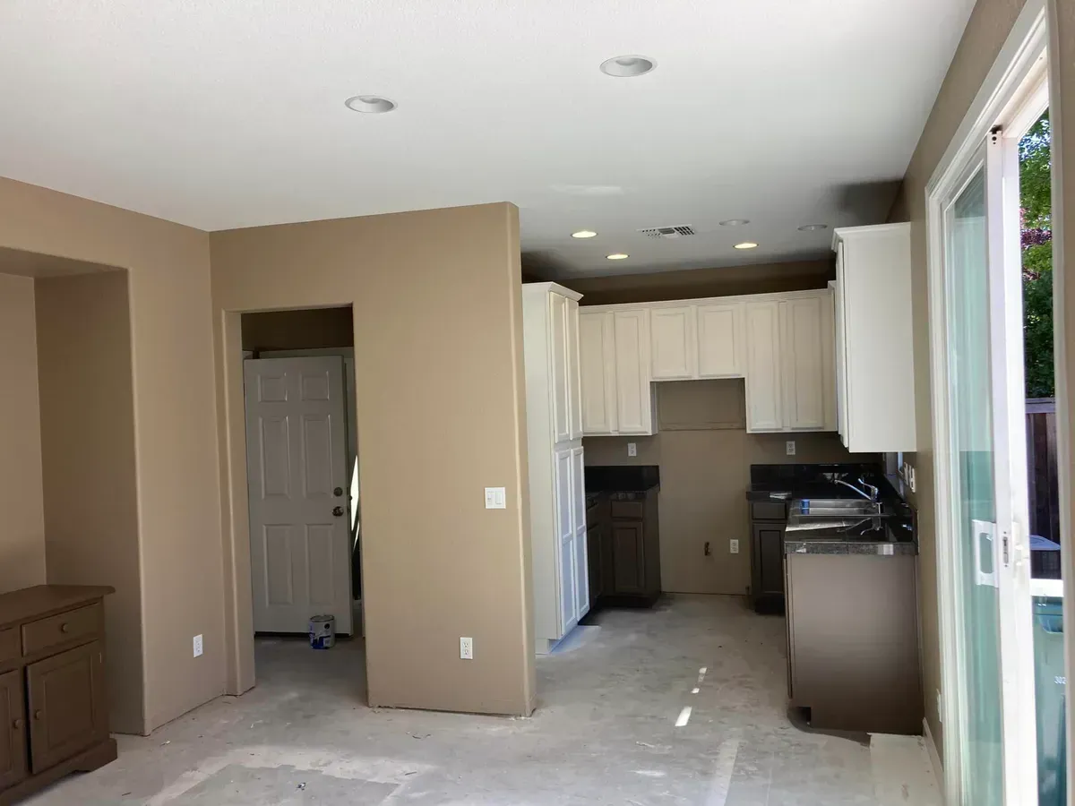 Beige kitchen under construction with white cabinets, a sliding glass door, and a hallway.