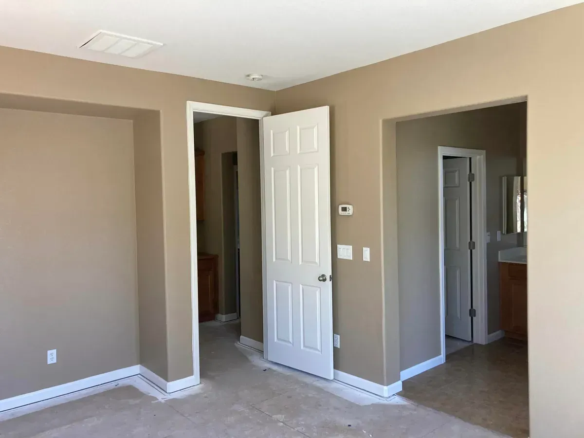 A beige room with a white door. Open doorways lead to other rooms, with white trim and beige walls.