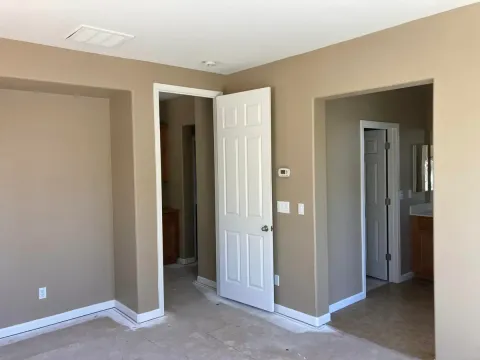 Empty bedroom with tan walls, white door and trim, doorway to bathroom.