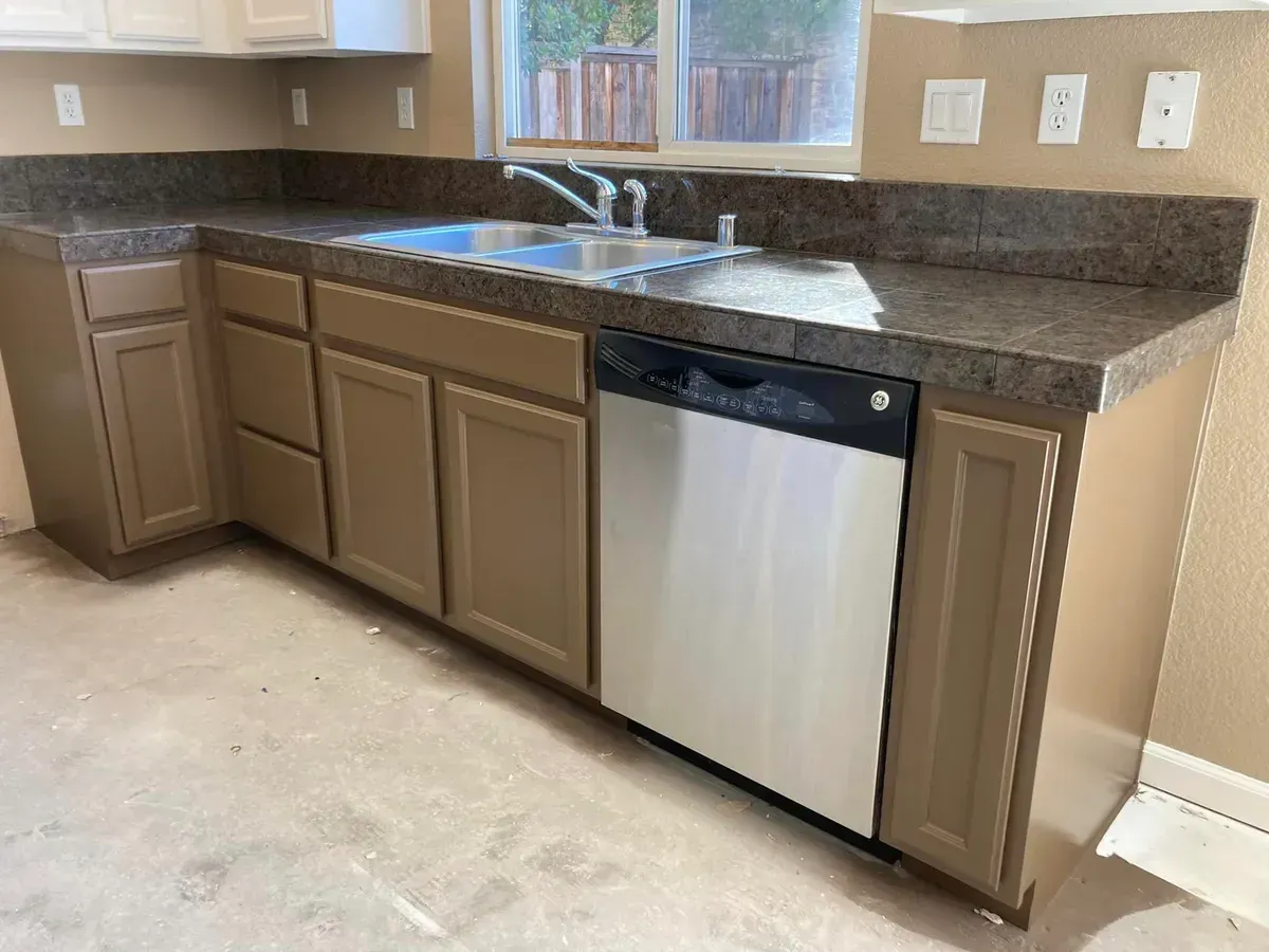 Kitchen with beige cabinets, dark countertop, stainless steel dishwasher, and sink.