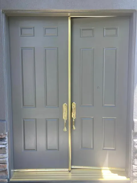 Double gray doors with gold handles and trim, set in a stone and stucco exterior.