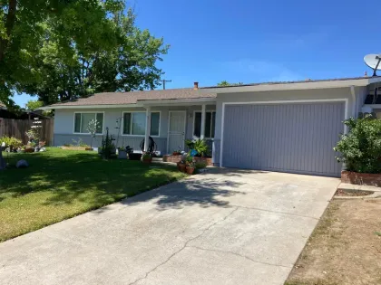 Gray ranch-style house with blue garage door and driveway on a sunny day.
