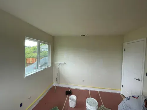 Room with newly painted beige walls, window, door, and painting supplies.