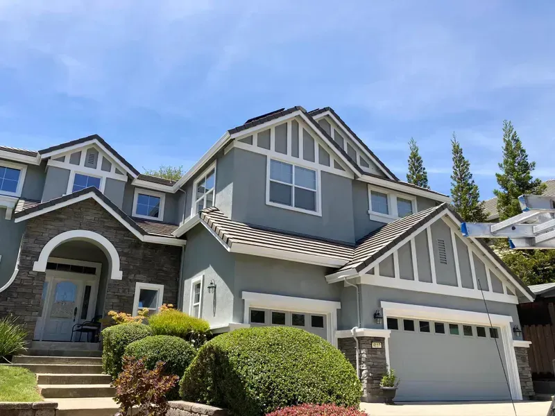 Two-story house with gray stucco walls, brown roof, stone accents, and a manicured front yard.