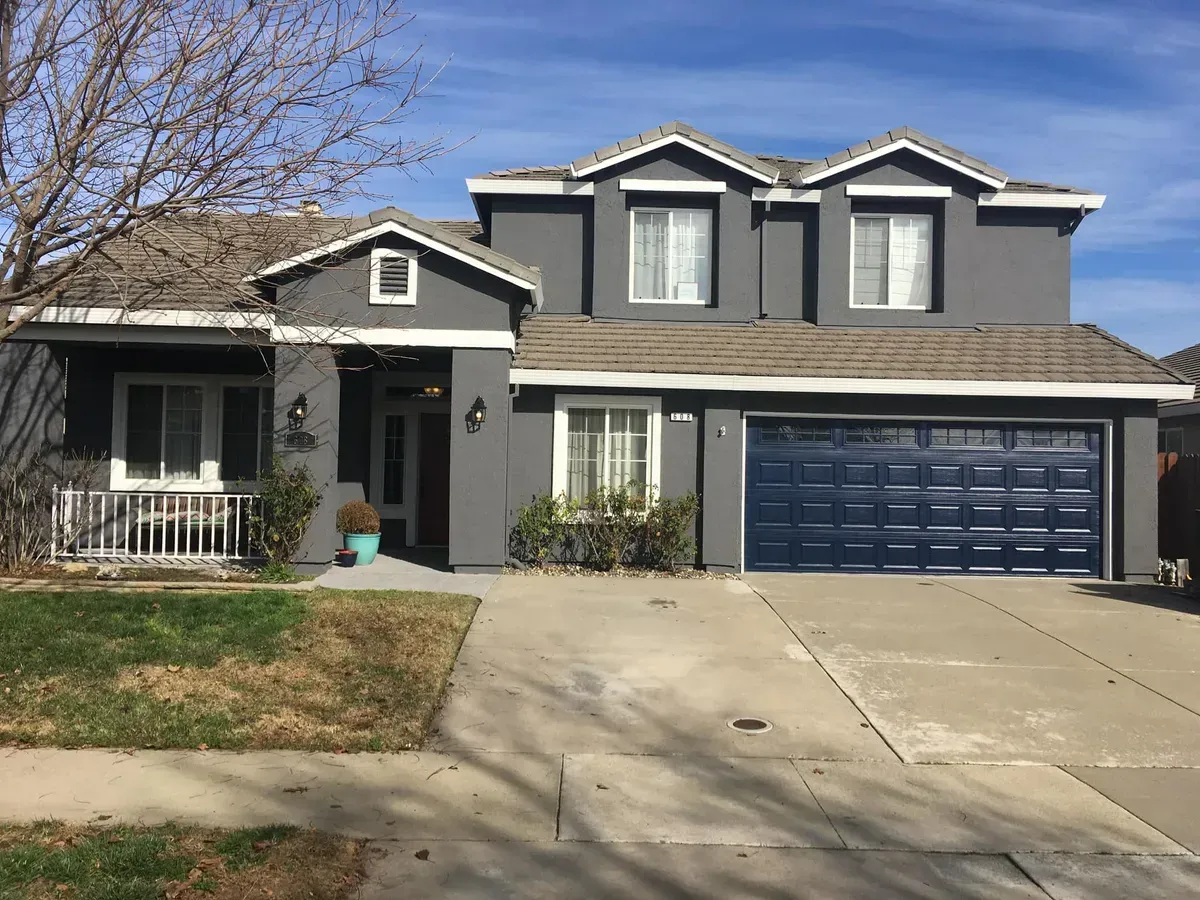 Gray two-story house with a blue garage door. Sunny day with a clear blue sky.
