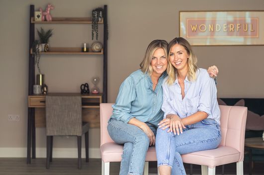 Helen and Ruth from Your Moving Day, a home unpacking company sat smiling together. They are both wearing denim and blue and have blonde hair.