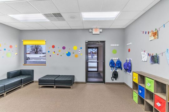 A room with a couch , shelves , and backpacks hanging on the wall.