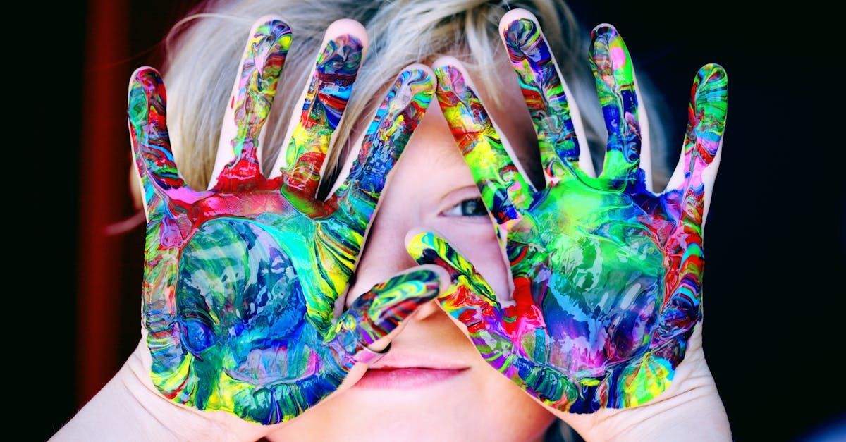 A child is covering his eyes with his hands painted in different colors.