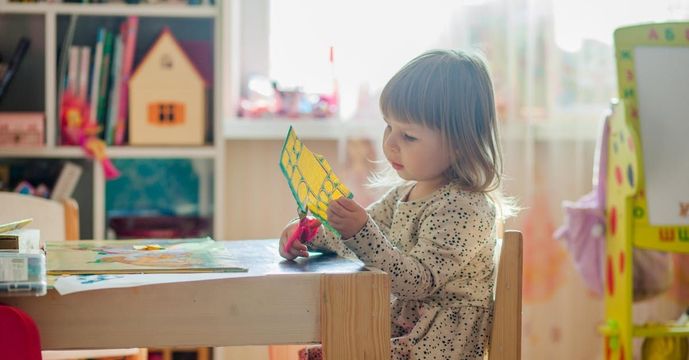 A little girl is sitting at a table holding a piece of paper.