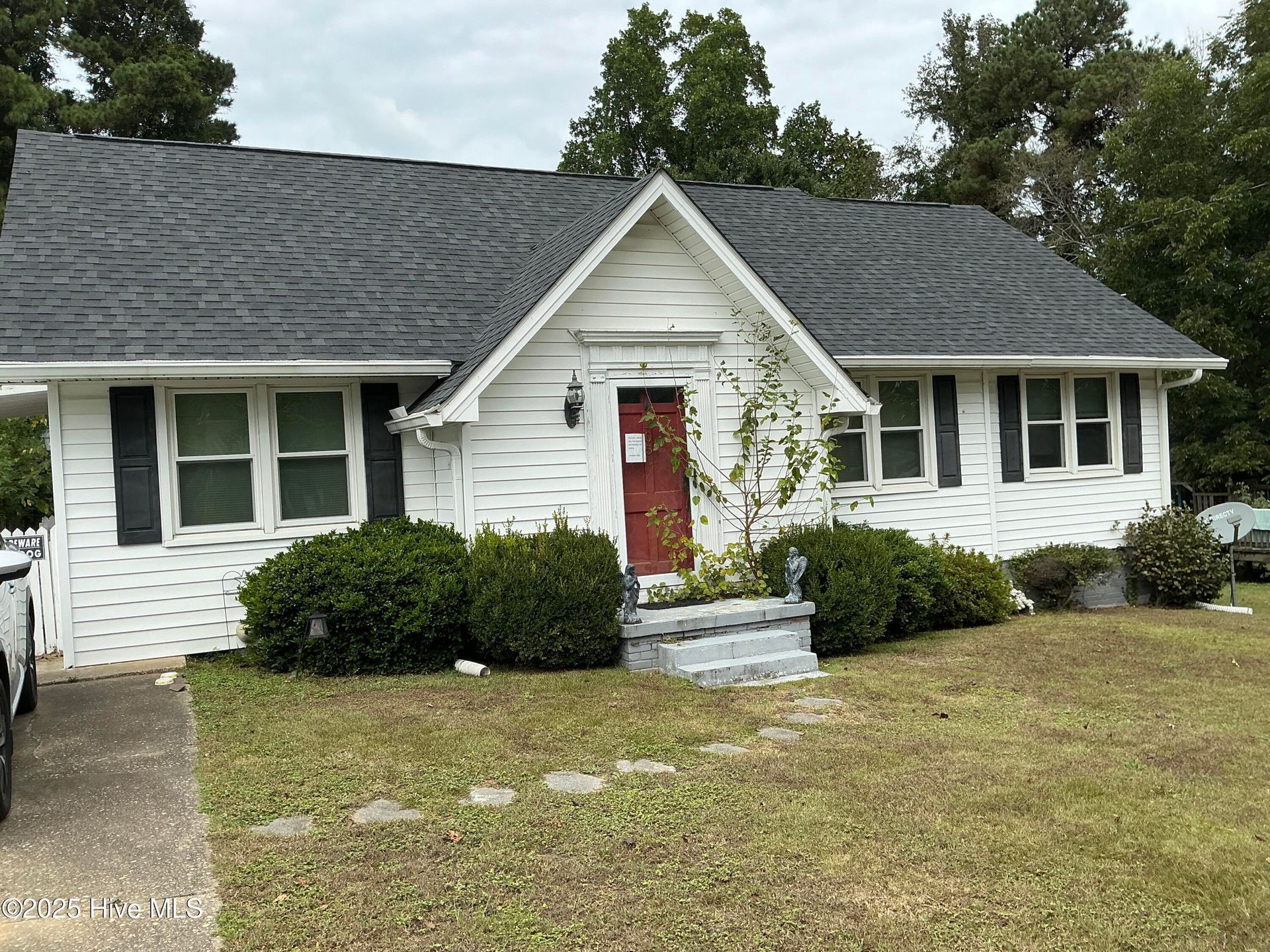 Single-story white house with a red front door, gray roof, shrubs, and a grassy yard
