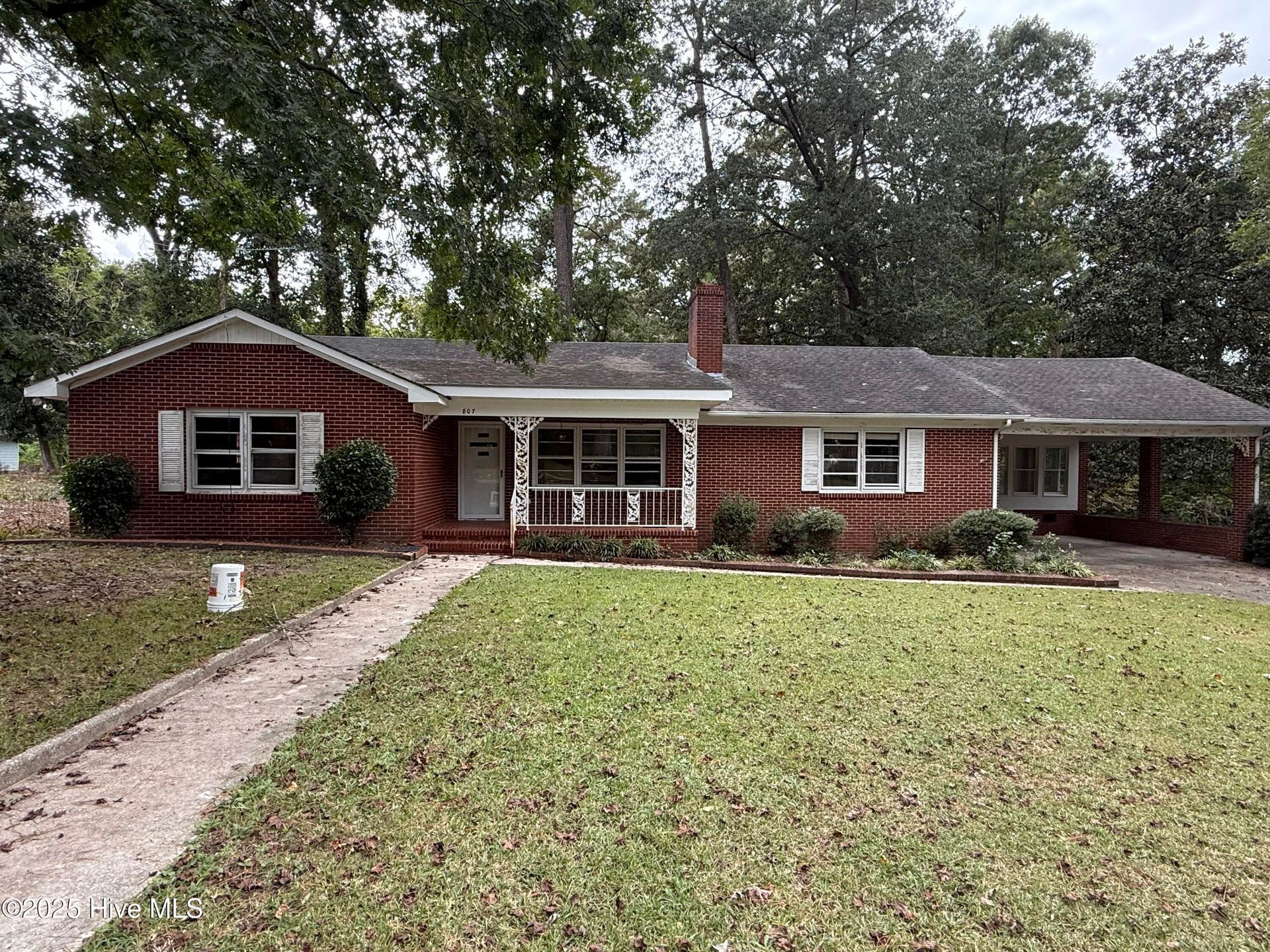 Single-story red brick house with a front porch, white trim, and a gravel driveway amid trees.
