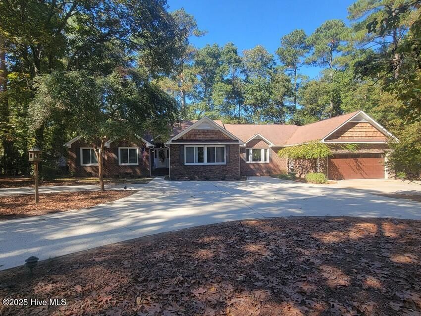 Single-story brick house with a two-car garage, curved driveway, and large trees in front yard