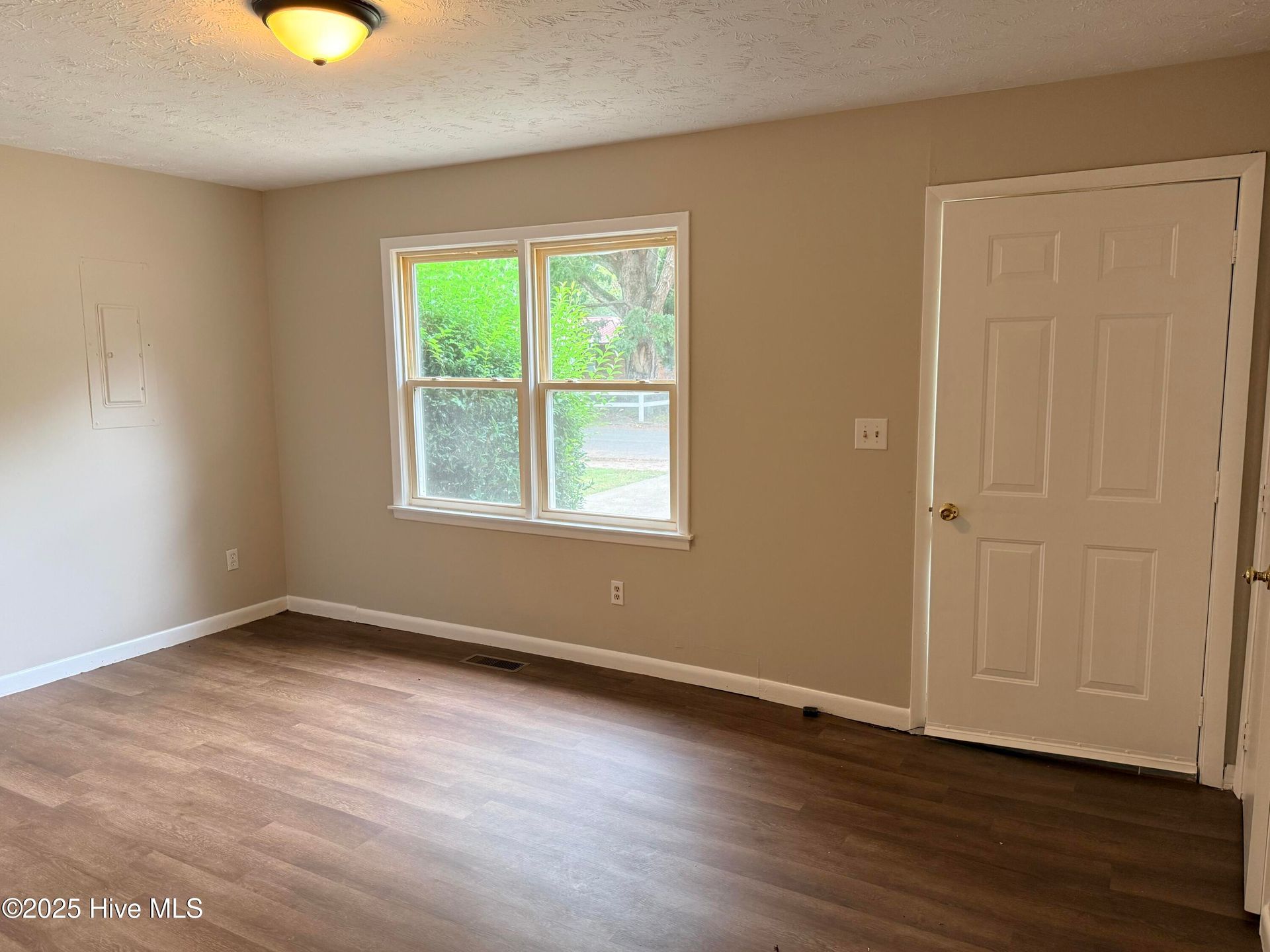Empty beige bedroom with wood floor, window, and white closet door