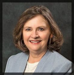 Portrait of a smiling woman in a light blue blazer against a dark gray backdrop