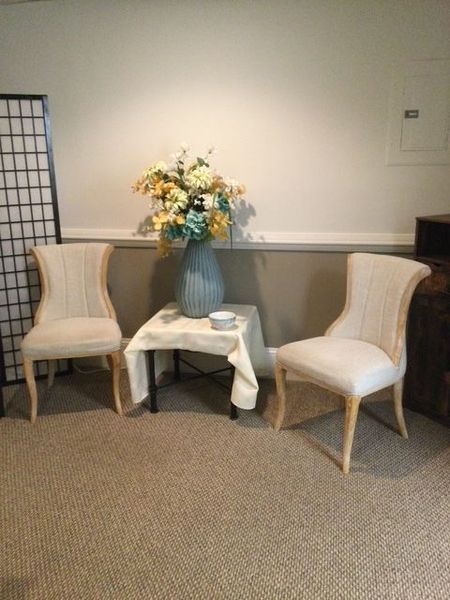 Two light-colored upholstered chairs flanking a small table holding a blue vase with flowers against a two-toned wall.
