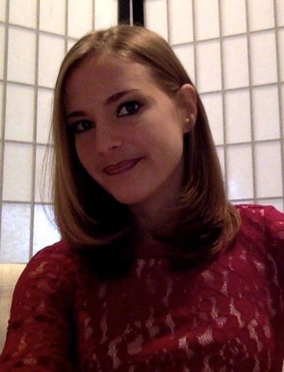 A woman in a red lace top looks toward the camera, standing in front of a white grid-patterned room divider.