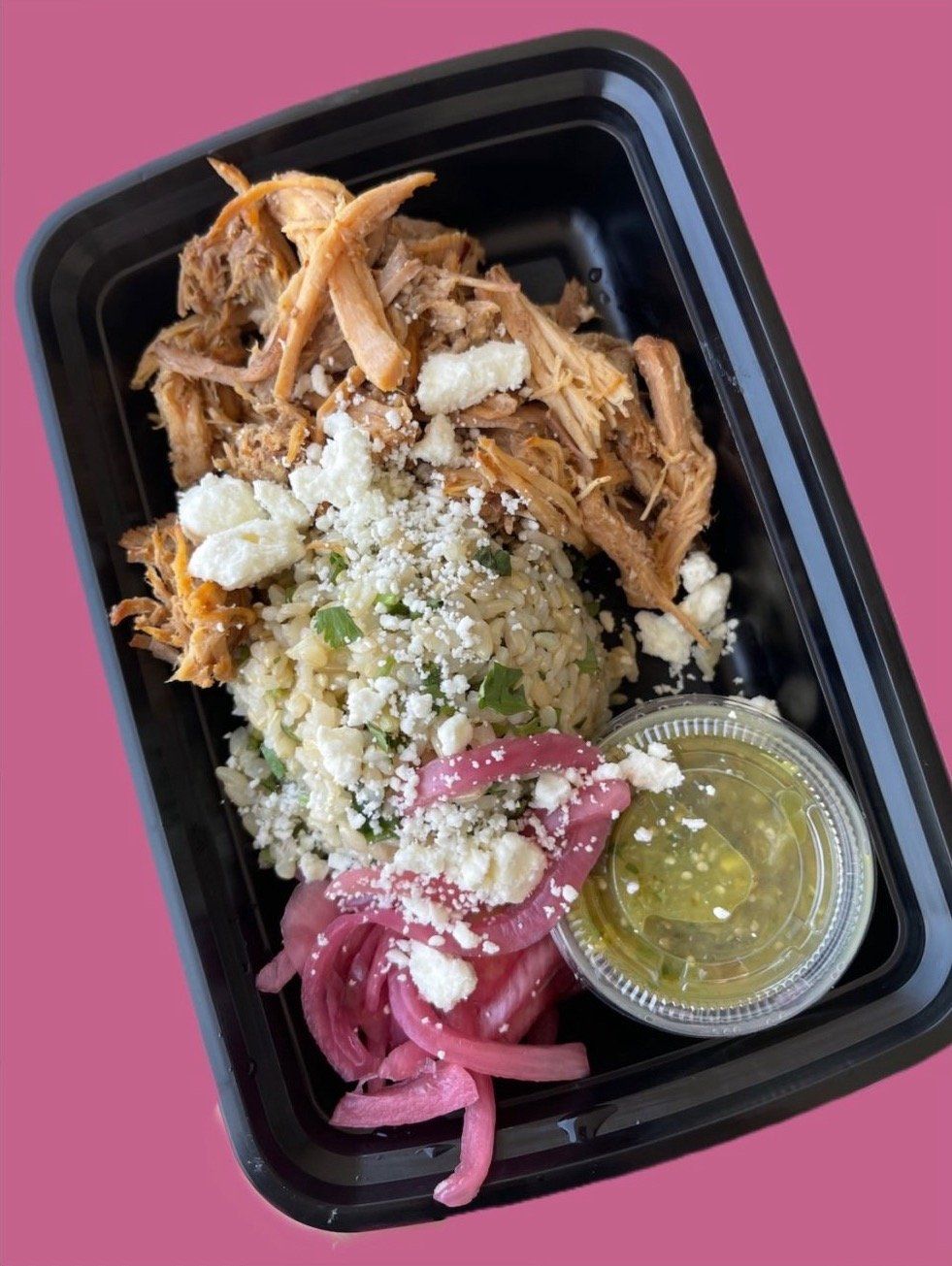 A black plastic container filled with chicken , rice , cheese , onions and a dipping sauce.